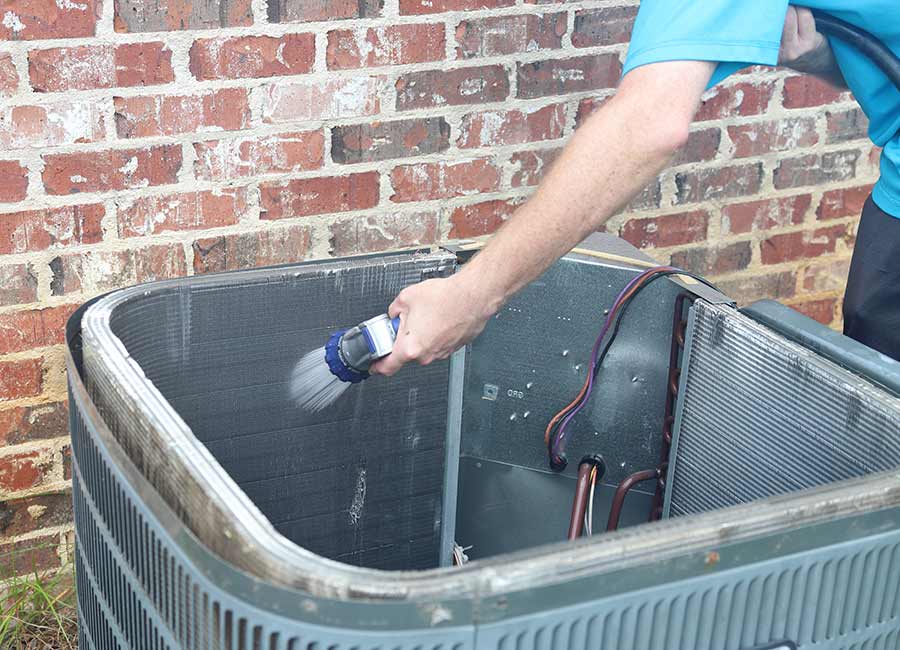Technician cleaning an outdoor AC unit coil with a water hose